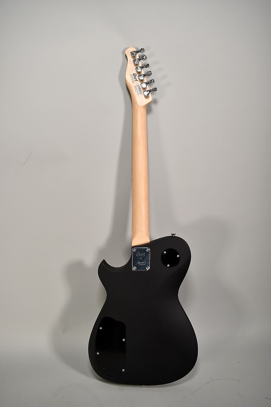 The back of a matte black electric guitar with a light wood neck, chrome tuners, and a chrome neck plate.