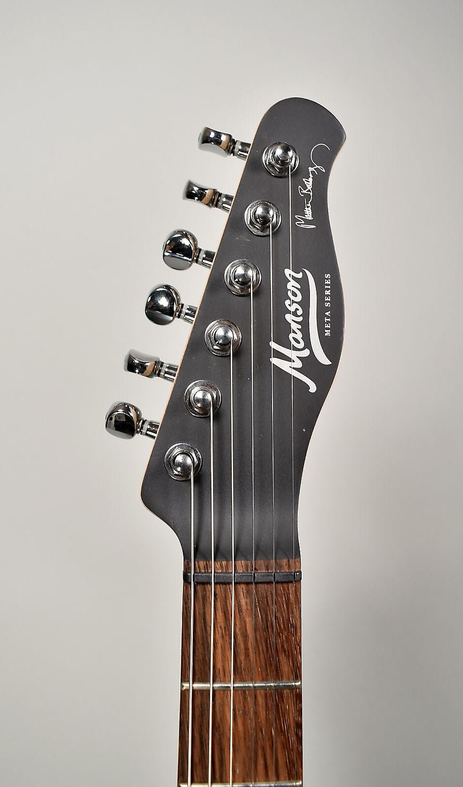 The guitar's headstock, angled slightly left, is matte black with chrome tuners and a dark wood fretboard.