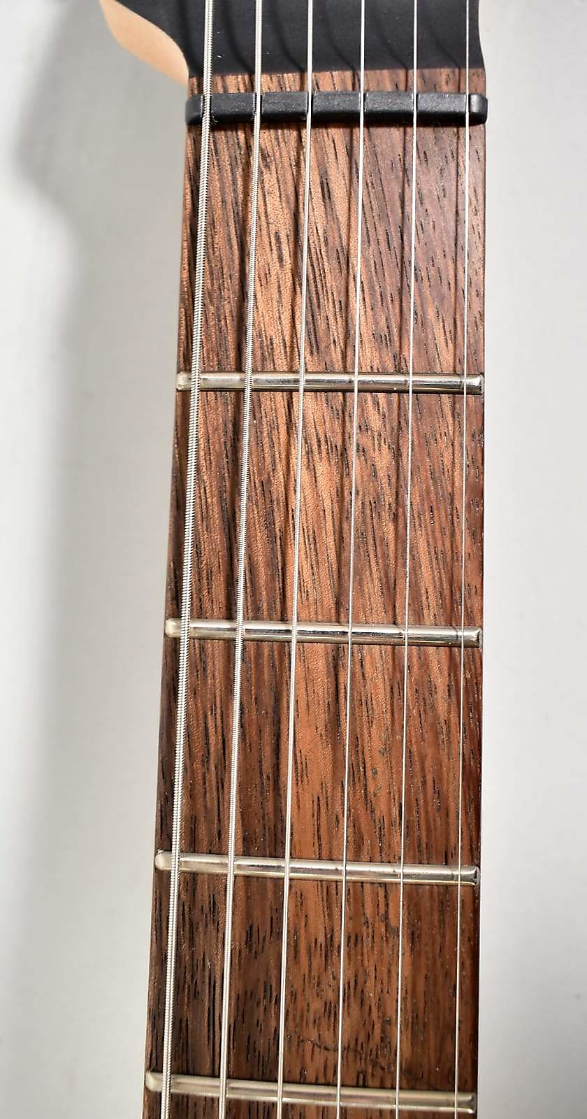 Close-up of the dark brown fretboard with prominent grain, silver frets, and six strings, viewed from the nut down.