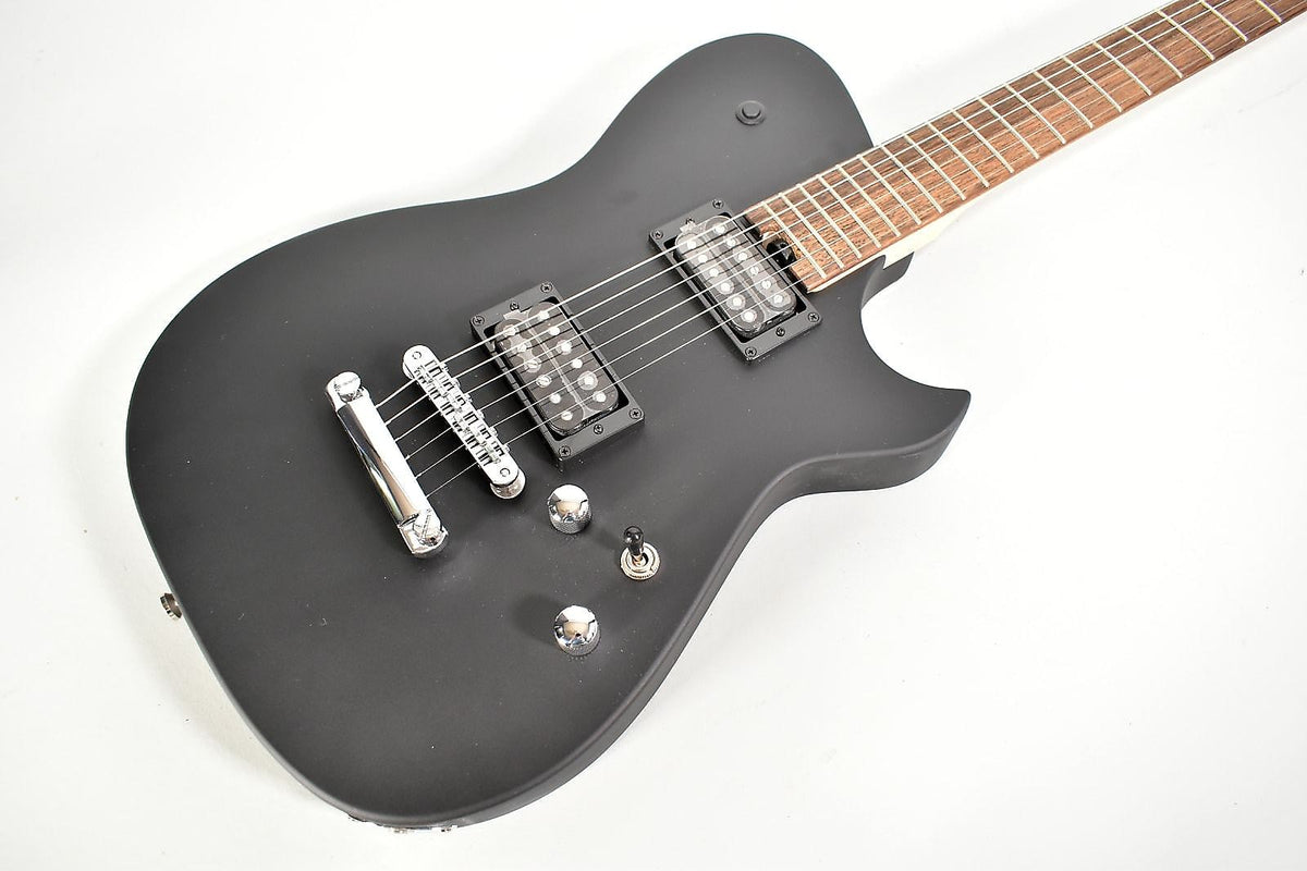 The matte black electric guitar is angled from the upper right, showing its body, two humbuckers, and chrome hardware.