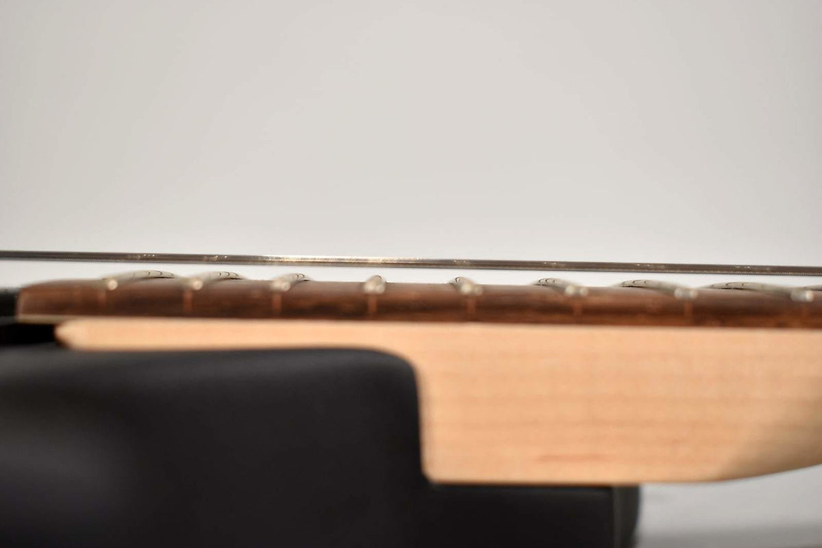 A close-up side view of the guitar neck, showing the light wood neck, dark fretboard, and metal frets and strings.