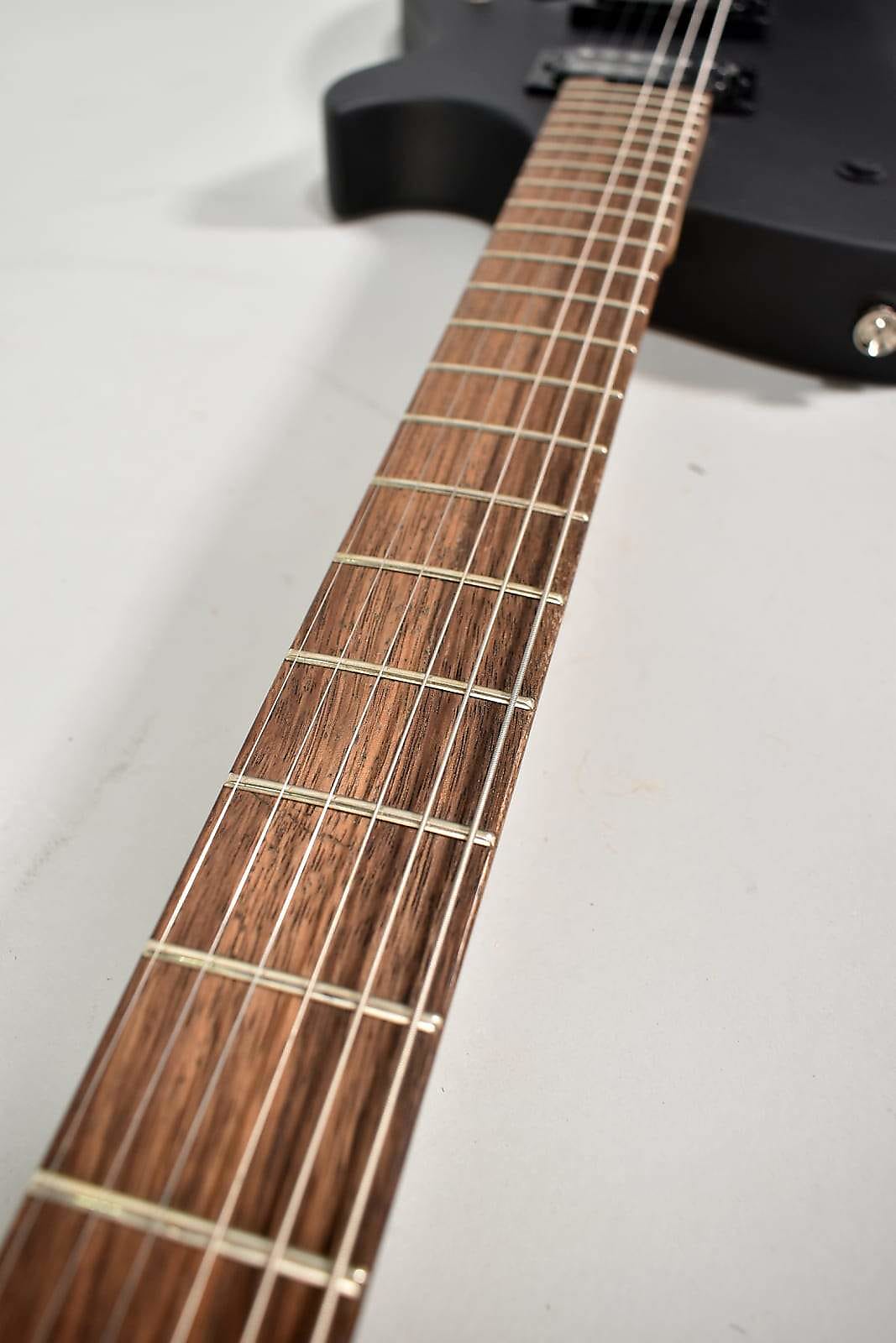 The guitar's dark brown fretboard with silver frets and strings is angled from the lower left, with the matte black body blurred in the background.